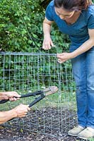 Two women using bolt cutters to remove a section of gabion basket