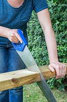 Close up detail of woman using saw to cut wooden plank to correct length