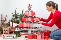 Woman hanging gifts bags on Advent pallet Christmas tree 