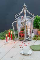 Christmas scene including miniature tree, red chair and lit candle in metal lantern. 