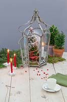Christmas scene including miniature tree, red chair and lit candle in metal lantern