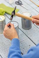 Woman using a hammer and a nail to create drainage holes in tin cans