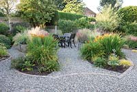 View of urban back garden with raised wooden flowerbeds, curving gravel paths and seating area.