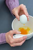 Woman blowing the content of the egg into a bowl leaving the shell empty