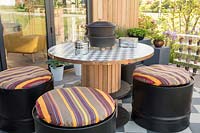 Repurposed wooden table with oil drum seats and cushions. 'At Home - Grow, Dine, Relax' garden, RHS Malvern Spring Festival, 2018.
