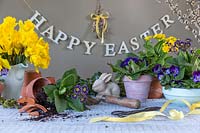 Easter arrangement with spring flowers, tools, pots, rabbit and a Happy Easter sign