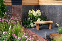 Brick path leading to a brick wall feature, wooden bench on slate tiles next to border with Hydrangea paniculata 'Phantom', Verbena bonariensis, Rosa 'Skylark' and Echinacea purpurea in foreground - A Place to Ponder, RHS Tatton Park Flower Show 2018