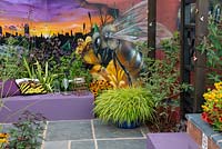 Mural of a worker bee by graffiti artist, Russ Meehan, seating area with Hakonechloa macra - The Buzz of Manchester, RHS Tatton Park Flower Show 2018