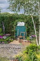 Chair next to a green garden gate with tools, brick patio and Betula underplanted with native ferns - 130 Years of Port Sunlight, The Garden Village, RHS Tatton Park Flower Show 2018