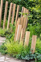 Timber posts framing a path between planting of lush green foliage of Seslaria autumnalis,  Dryopteris felix-mas, Vinca minor 'Gertrude Jekyll' and Astrantia major 'Large White' - Calm in Chaos, RHS Tatton Park Flower Show 2018