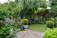 Borders in a small urban garden with paved area, shady lawn under a silver birch, Betula Pendulum 'youngii'