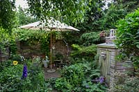 Cream parasol stands on patio area of small urban garden. 