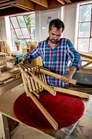 Chris Punch, garden furniture designer, in his workshop assembling a footstool from component parts. 