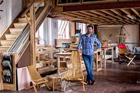 Chris Punch, garden furniture designer in workshop, with range of chairs.
