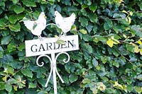 Decorative cut metal garden sign against a beech hedge.