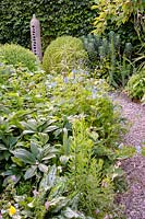 View of gravel path leading between mixed perennial borders. 