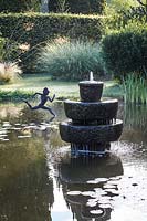 Tiered stone fountain in lake with sculpture in background