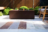 Rusted elements in the garden like fireplace, panel walls and paving in small contemporary garden. 