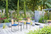 Wooden table and chairs with raised bed of Echinacea, Salvia and Stipa, RHS Hampton Court Palace, 2018.
