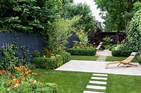 Garden design by Nick Gough 
Overview of garden with artificial lawn with stone slab path and patio with 
wooden chairs. Planting on the left: buxus sempervirens hedge 
Orange Helenium 'Moerheim Beauty' 
Yellow Achillea 'Teracotta'  
Pink Cirisium riv. Altropurpureum