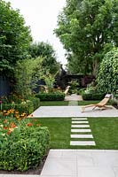 Garden design by Nick Gough 
Overview of garden with artificial lawn with stone slab path and patio with 
wooden chairs. Planting on the left: buxus sempervirens hedge, 
Orange Helenium 'Moerheim Beauty', 
Yellow Achillea 'Teracotta'  
Pink Cirisium riv. Altropurpureum