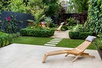 Garden design by Nick Gough 
Overview of garden with artificial lawn with stone slab path and patio with 
wooden chairs. Planting on the left: buxus sempervirens hedge 
Orange Helenium 'Moerheim Beauty' 
Yellow Achillea 'Teracotta'