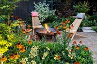 Garden designed by Nick Gough Gravel patio area with wooden chairs with logs burning in log burnerBorder planting includes:Acer palmatum Katsurabuxus sempervirens hedge Orange Helenium Moerheim Beauty Yellow Achillea Teracotta