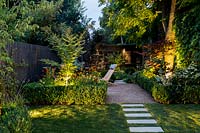 Illuminated borders with path on artificial lawn and Buxus sempervirens hedge 