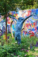 The Supershoes, Laced with Hope Garden, sculpture of boy with arms outstretched, by Alison Bell, under a cherry tree - Prunus maackii, colourful graffiti wall behind, painted by Karen Huwen - RHS Chelsea Flower Show, 2018 - Sponsor: Frosts Garden Centres