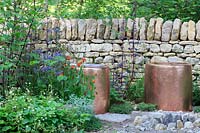 Copper seats and a fire-pit, backed by a drystone wall. The Warner Edwards Garden, a representation of Falls Farm in the Northamptonshire countryside, Sponser: Warner Edwards, RHS Chelsea Flower Show, 2018.

