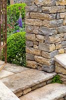 Stone steps and wall of formal show garden. A Very English Garden. Sponsor: The Claims Guys, RHS Chelsea Flower Show, 2018. 