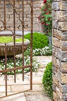 Rusty gate with view to garden behind. A Very English Garden. Sponsor: The Claims Guys, RHS Chelsea Flower Show, 2018.

