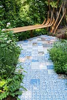 Bench and patterned tile path in show garden. The Embroidered Minds Epilepsy Garden. Sponsor: Embroidered Minds, RHS Chelsea Flower Show, 2018.

