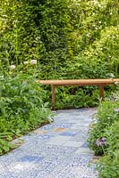 Ceramic tile path by Sue Ridge, surrounded by planting leading to wooden bench. The Embroidered Minds Epilepsy Garden. Sponsor: Embroidered Minds, RHS Chelsea Flower Show, 2018.

