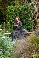 Girl in Nineteenth Century long dark dress reading in The Embroidered Minds Epilepsy Garden - Sponsor: Embroidered Minds - RHS Chelsea Flower Show 2018