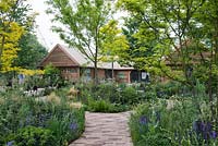 Brick path leading between borders full of grasses and perennials, with Gleditsia triacanthos - Honey Locust Tree - The RHS Feel Good Garden, RHS Chelsea Flower Show 2018