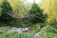 Metal sculpture over natural stone paving and pool with Salix alba 'Tristis' and Iris 'Carnival Time' - The Wedgwood Garden - RHS Chelsea Flower Show 2018