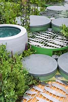 Pond in round container and path made of circular stepping stones with metal grates with pea shapes - The Seedlip Garden - Sponsor: Seedlip - RHS Chelsea Flower Show 2018