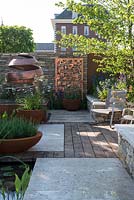 Weathered oak decking leading to Purbeck walling with copper panels, lasered to reflect the Silent Pool Gin pattern - The Silent Pool Gin Garden - Sponsor: Silent Pool Distillers - RHS Chelsea Flower Show 2018