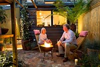 Owners Emma and Brian sitting next to fire bowl in their small London patio garden 