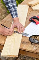 Man using a ruler to measure and mark a cut on a wooden board.