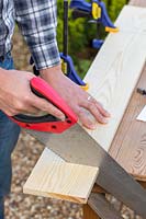 Man using a saw to cut  a wooden board. 