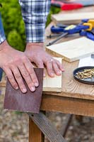Man using sandpaper to smooth the edge of newly cut wood.