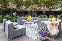 Grey outdoor sofa arrangement with yellow cushions, tables, drinks and rug
