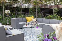 Grey outdoor sofa arrangement with yellow cushions, tables, drinks and rug. 