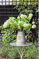Floral arrangement of artificial Snowball flowers in vintage metal container on table. 