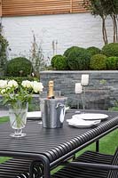 Outdoor table set with white roses, candles and champagne bottle in cooler