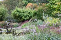 Dragon sculpture in round pool surrounded by densely-planted borders of grasses, perennials and trees.