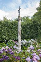 Tall, stone column in Hydrangea garden, surmounted by lead, classical figure