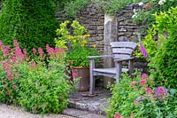 View of wooden chair surrounded by flowering plants, Hanham Court Gardens, Bristol, UK. 